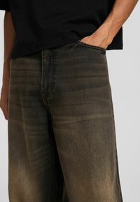 Lös passform jeans i blekt svart denim. Har subtila blekningsmönster, femfickorsdesign och synlig sömnad längs sömmarna.