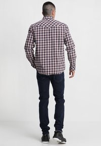 Camicia a maniche lunghe a quadri con motivo rosso, blu e bianco, realizzata in cotone. Abbinata a jeans blu scuro e scarpe da ginnastica nere.