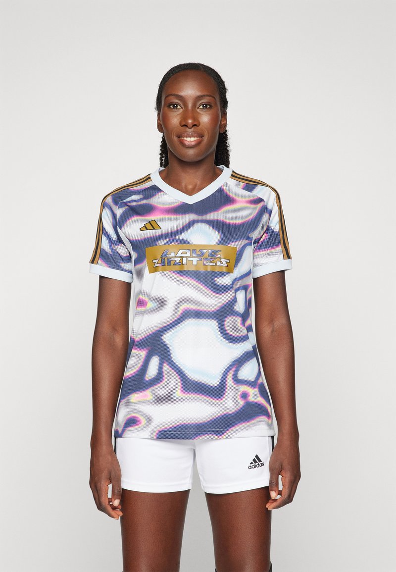 Frauenfußballtrikot in Weiß, Lila und Gold; mit einem wellenförmigen abstrakten Muster, V-Ausschnitt und drei goldenen Streifen auf den Schultern.