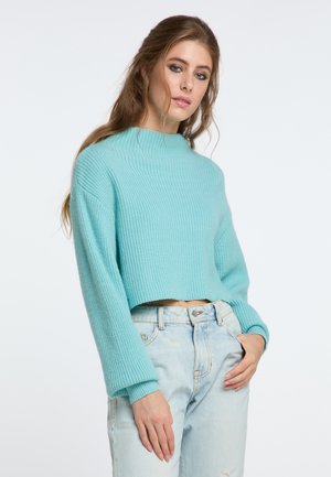 Crochet-style, short-sleeve sweater in light turquoise with a ribbed texture. Paired with high-waisted, distressed light blue jeans.