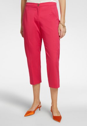 Pantaloni cropped rosa con taglio dritto, chiusura con bottone e tasche laterali, abbinati a décolleté arancioni con punta a punta.