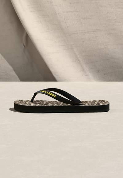 Sandale tong noire avec semelle intérieure imprimée léopard et brides noires ornées du logo jaune "DSQUARED2", posée sur une surface et un fond clairs.