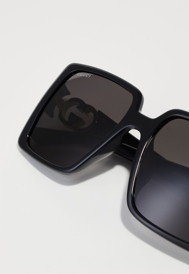 Schwarze übergroße quadratische Sonnenbrille mit dunklen Gläsern, die ein schwaches Gucci-Logo auf dem oberen linken Glas und ein doppeltes G-Emblem im Glas zeigen.
