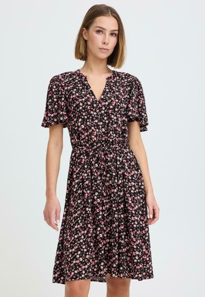 Woman wearing a black knee-length dress with pink floral print, short flutter sleeves, and a cinched waist with a tie belt.