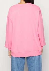 Pink sweatshirt with dropped shoulders, ribbed cuffs, and hem. Soft cotton fabric, relaxed fit, and smooth texture. No patterns or accents.