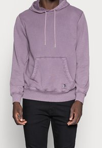 Lila hoodie med en framficka, dragskohuva, ribbade ärmslut och fåll. Har en logotypetikett på fickan. Mjuk tygtextur.