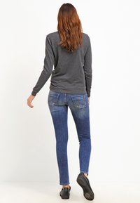 Maglietta grigia a maniche lunghe abbinata a jeans skinny blu medio. I jeans presentano due tasche posteriori e una leggera scoloritura, completati da scarpe nere.