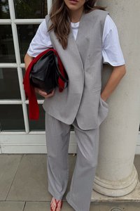 Ljusgrå kostym med en ärmlös, skräddarsydd väst och vida byxor. Kombineras med en vit t-shirt, en röd scarf och en svart handväska.