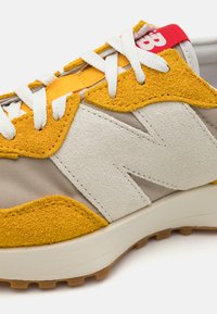 Sneaker mit oberem Teil aus beigem Mesh, gelben Wildlederakzenten und weißen Schnürsenkeln. Besitzt ein markantes 'N'-Design, Retro-Stil und ein rotes Etikett.