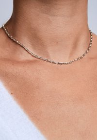 Zilveren ketting gemaakt van langwerpige schakel met een gladde, gepolijste afwerking, rustend op een lichte huidtint.