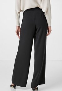 Wijdbenige zwarte broek van een gladde stof, hoge taille en keurig aangepaste naden. Gecombineerd met een lichtgekleurde, loszittende top.
