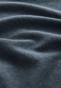 Tmavomodrý textil s hladkým, textúrovaným povrchom, ktorý má jemné záhyby a subtilné variácie odtieňov. Ľahký a flexibilný materiál.