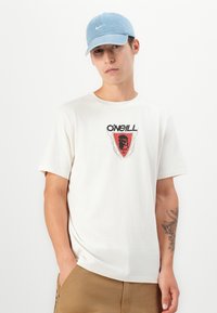 Cream short-sleeve t-shirt with black and red O'Neill logo, paired with khaki shorts. Worn with a light blue cap featuring a white logo.