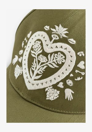 Olive green cap featuring white embroidery of a heart-shaped design with floral motifs, hands, and decorative elements.