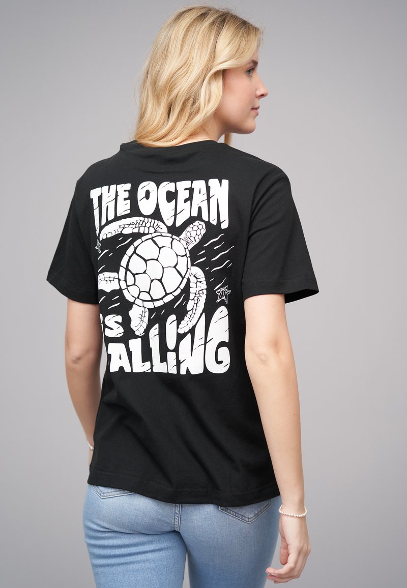 Black cotton t-shirt featuring a large white graphic of a turtle and text reading "THE OCEAN IS CALLING" on the back. Short sleeves, casual fit.