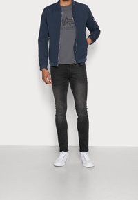 Navy bomber jacket with ribbed cuffs, gray logo t-shirt, black skinny jeans, and white sneakers; smooth fabric, simple design.