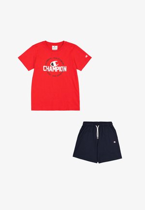 Camiseta de algodón roja con el logo "CHAMPION" en blanco, combinada con pantalones cortos azul marino que tienen una cintura elástica y bolsillos laterales.