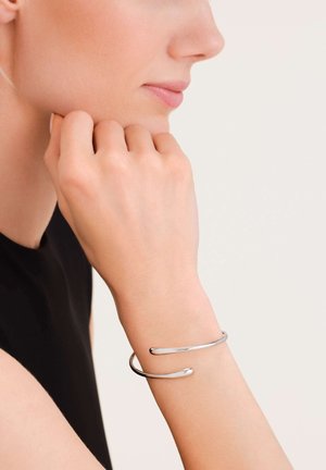 Bracciale in argento con un design semplice e minimalista, caratterizzato da un'apertura a fessura e una finitura lucida, indossato a un polso.