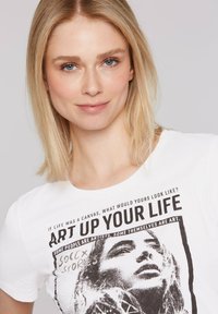 Biała bawełniana koszulka z odważnym czarnym nadrukiem z napisem "ART UP YOUR LIFE" oraz artystyczną grafiką twarzy kobiety.