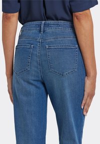 Blå denimjeans med hög midja, utrustade med två bakfickor och en slät yta. Tyget har en lätt urblekt finish.