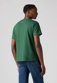 Groene katoenen T-shirt met korte mouwen, ronde hals, ontspannen pasvorm en een gladde textuur, gecombineerd met blauwe jeans. Achteraanzicht weergegeven.