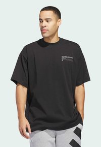 Camiseta negra de gran tamaño hecha de algodón, con cuello redondo y un pequeño gráfico en el pecho. Combinada con pantalones de chándal grises.