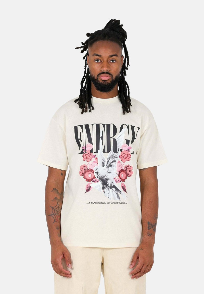 Lichtbeige t-shirt met een grafische print van een vogel en bloemen, met vette zwarte tekst "ENERGIE." Gemaakt van zachte katoen, met een relaxed fit.