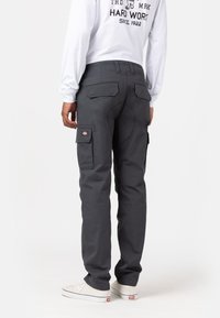 Grijze cargobroek met een relaxte pasvorm, meerdere zijzakken en een gestikt naaddesign, gecombineerd met casual witte schoenen.