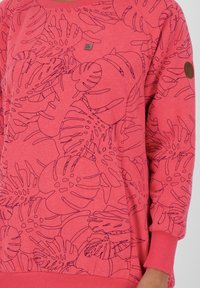 Felpa rosa con un motivo floreale in artigianato a linea nera, con polsini e scollo a costine. Piccolo dettaglietto a forma di badge sul petto.