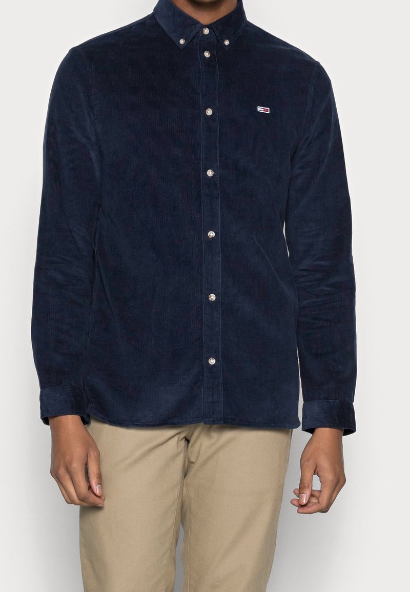 Tmavě modrá košile z manšestru s límečkem na knoflíky, s malým logem na hrudi, stříbrnými knoflíky a dlouhými rukávy s manžetami na knoflíky.