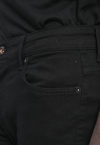 Jeans negri din denim cu un design slim, având o buzunar frontal, detalii cu nasture cu tonalitate de cupru și o textură subtilă.