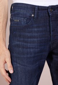 Tmavě modré džínové kalhoty s hladkým povrchem, vybavené přední kapsou s malým logem BOSS a klasickým pěti-kapsovým designem.