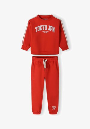 Ensemble sweat-shirt et pantalon de jogging rouge avec le texte blanc "TOKYO JPN", des rayures sur les manches et une taille élastique avec cordon de serrage.