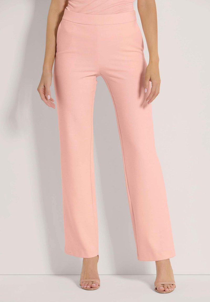 Lichtroze uitlopende broeken van een soepel, rekbaar materiaal met een brede tailleband. De broek heeft een strakke uitstraling zonder versieringen.