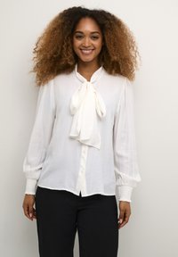 White, long-sleeve blouse with a bow tie neck, button front, and gathered cuffs. The fabric appears smooth and lightweight.