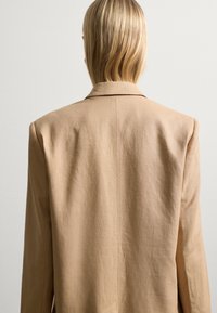 Beiger Leinen-Blazer mit taillierter Passform, Reverskragen und sauberem Rückennaht. Verfügt über eine weiche Textur und minimalistische Details.