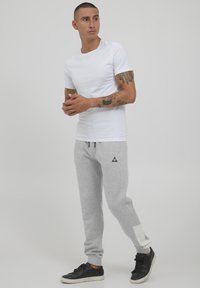 White short-sleeve t-shirt, gray sweatpants with a white accent at the cuff, and black sneakers. Simple design with a relaxed fit.