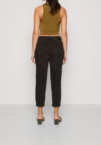 Jeans negros de tiro alto con corte recto, dos bolsillos traseros y un ligero ceñido en el tobillo. Combinados con una camiseta sin mangas oscura y sandalias.