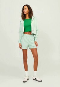 Um hoodie cropped verde menta e calções iguais, com uma blusa verde justa por baixo. A modelo usa meias brancas e sapatilhas com detalhes em preto.