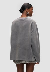 Sweatshirt grigio oversized con una texture morbida, spalle scese e scollatura rotonda. Abbinato a una gonna a fantasia bianco e nero.
