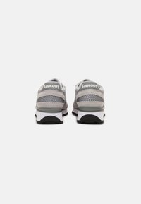 Grijze sportschoenen van mesh en suède, met een witte tussenzool, zwarte buitenzool en het "Saucony"-logo op de hiel.