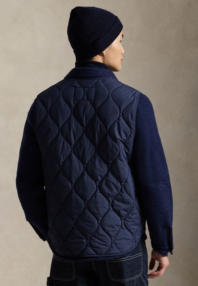 Μπλε στιβαρό γιλέκο με υφασμένα μάλλινα μανίκια, με μοτίβα ρόμβων και γιακά. Συνδυάζεται με ταιριαστό πλεκτό σκούφο.