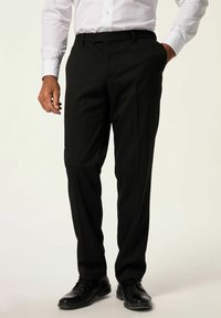 Pantaloni neri su misura con davanti piatto, passanti per la cintura e una texture liscia, abbinati a scarpe da uomo nere lucide su uno sfondo chiaro.