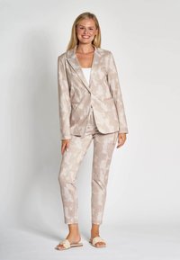 Light beige suit with a camouflage pattern, tailored blazer and slim-fit trousers, made from a textured fabric, paired with tan slip-on sandals.