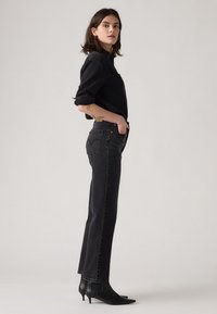 Zwarte denim jeans met een rechte pijp en een hoge taille. Gecombineerd met een zwart langemouwen shirt en zwarte puntige enkellaarsjes.