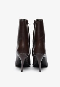 Brown leather ankle boots with a sleek design, high stiletto heels, and a back zipper detail. Smooth texture with a minimalistic finish.