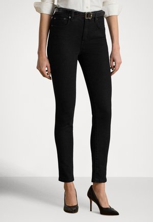 Jean noir slim porté avec une chemise blanche rentrée, ceinture noire et chaussures à talons hauts noires.