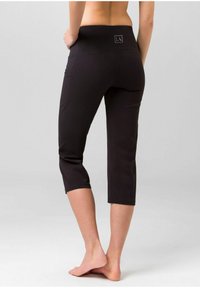 Schwarze, taillierte Leggings mit breitem Bund, die ein kleines Logo auf der Rückseite haben, aus glattem Material bestehen und am Wadenrand tapered geschnitten sind.