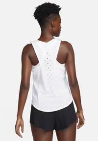 Débardeur de sport blanc avec encolure arrondie, trous de ventilation au dos et ourlet incurvé. Assortie à un short noir plissé.
