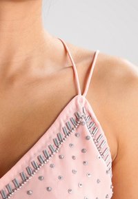 Rosa tygtop med tunna remmar, prydd med silverpärlor och avlånga metallaccenter längs halsringningen och fållen. Slät textur.